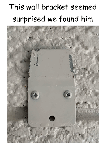 A wall bracket has two screws which appear as eyes, and a hole for a third screw at the bottom looks like an open mouth, creating the illusion of a surprised face
